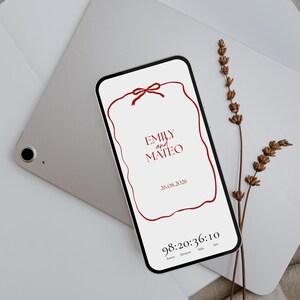 May include: A smartphone displays a wedding invitation with the names "Emily and Mateo" and the date "26.08.2026" in burgundy. A burgundy ribbon design frames the text. A timer counts down the days, hours, minutes, and seconds. Dried lavender and a tablet are in the background.
