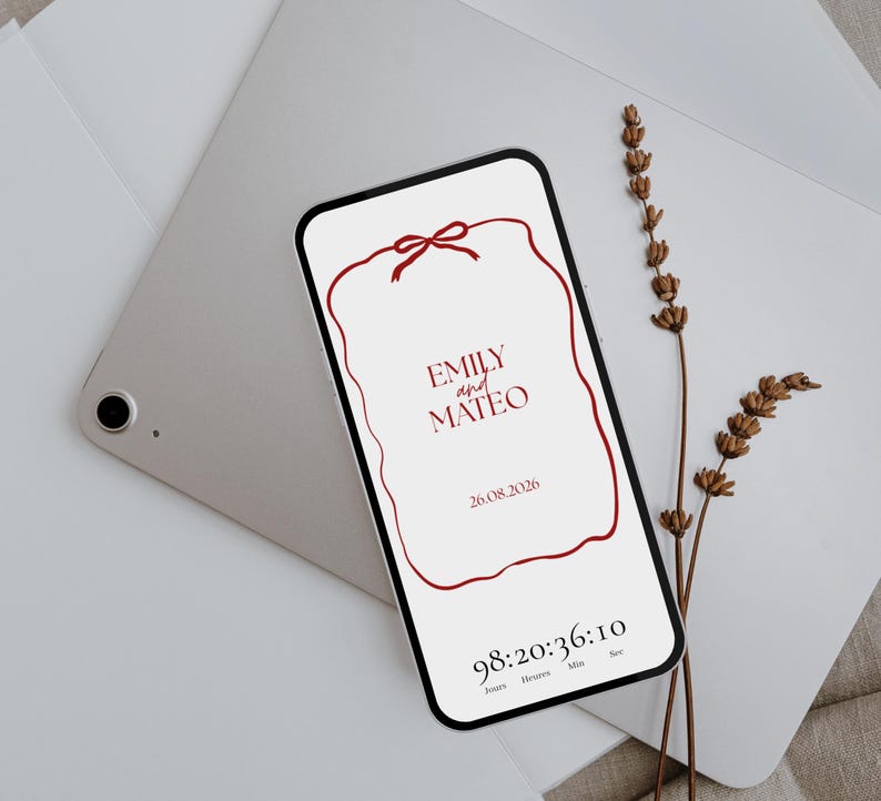 May include: A smartphone displays a wedding invitation with the names "Emily and Mateo" and the date "26.08.2026" in burgundy. A burgundy ribbon design frames the text. A timer counts down the days, hours, minutes, and seconds. Dried lavender and a tablet are in the background.