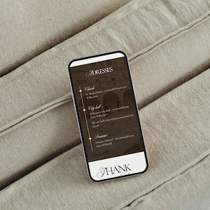 May include: A smartphone displays a list of addresses for dresses, including a church, city hall, and a domaine. The screen has a dark background with white text and a decorative font. The phone is on a beige fabric surface.
