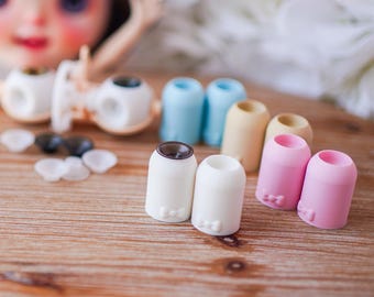 May include: A collection of small, cylindrical doll shoe components in various pastel colors including white, pink, beige, and light blue. Each piece features a subtle embossed bow detail at the base and a circular opening at the top for assembly.