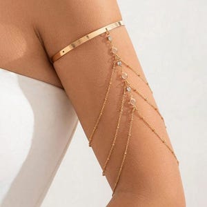 May include: Gold arm chain with multiple strands and small clear stones. The chain is designed to be worn on the upper arm.