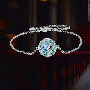 May include: Silver bracelet with a circular pendant depicting a tree and owl. The pendant has a colourful, iridescent background with blue, green, and red accents. The bracelet features a delicate chain and a secure clasp.