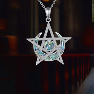 Puede incluir: Collar con colgante plateado con un diseño de estrella de cinco puntas, media luna y nudo celta. El colgante tiene un símbolo de triskele central y está adornado con detalles iridiscentes azules y verdes. El collar cuelga de una delicada cadena.