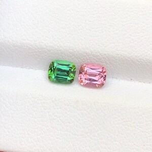 Può includere: Due pietre preziose, una verde e una rosa, sono esposte su uno sfondo bianco. Le pietre preziose sono rettangolari con angoli arrotondati. La pietra verde ha una tonalità smeraldo vibrante, mentre la pietra rosa è di un colore rosato tenue.
