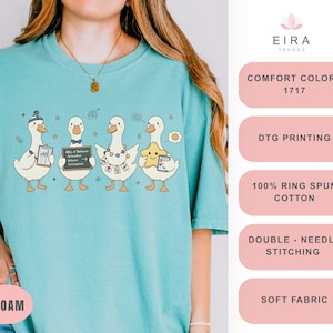 May include: Sea foam green t-shirt featuring a cartoon design of four ducks, each holding different items. The ducks are wearing hats, bow ties, and necklaces. The text "EIRA TRENDS" is at the top.