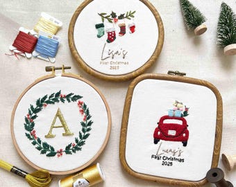 Può includere: Tre cerchi ricamati con cornici in legno. Uno presenta un design di calza natalizia, il secondo una ghirlanda con la lettera "A" e il terzo un'auto rossa che trasporta regali. Il testo include "Lisa's First Christmas 2025" e "Lucas's First Christmas 2025".