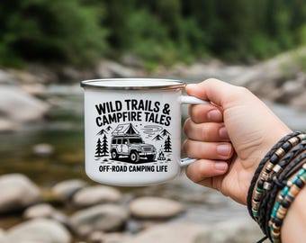 May include: White enamel camping mug with the text "WILD TRAILS & CAMPFIRE TALES" and an illustration of an off-road vehicle with a rooftop tent, trees, and a campfire. The mug is held by a person with bracelets.