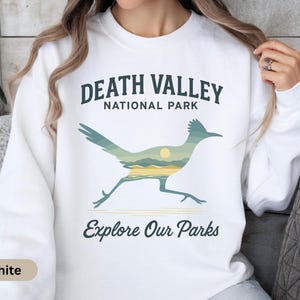 May include: White sweatshirt with a roadrunner graphic and a desert landscape design. The text "Death Valley National Park" and "Explore Our Parks" are printed above and below the roadrunner illustration.