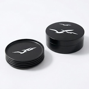 May include: A set of six black ceramic coasters and a matching round box. Each coaster and the box lid feature a white stylized bird design. The coasters are stacked, and the box is open.