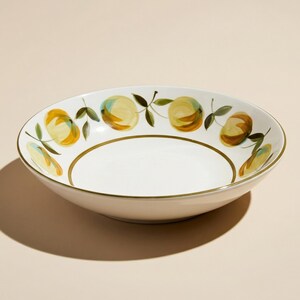 May include: White ceramic serving bowl with a hand-painted design of yellow and orange fruit with green leaves. The bowl has a gold rim and a wide, shallow shape, perfect for salads or pasta.