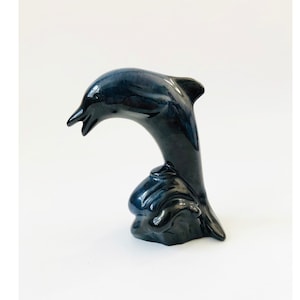 May include: A black ceramic dolphin figurine leaping out of the water. The dolphin is in a jumping pose with its tail curved and its head tilted back.