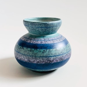 Op de afbeelding: Een keramische vaas met een bolvormige basis en een kleinere, uitlopende bovenkant. De vaas heeft horizontale strepen in tinten blauw, blauwgroen en lavendel. Het getextureerde oppervlak voegt visuele interesse toe aan dit decoratieve stuk.