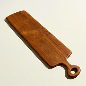 May include: A rectangular wooden serving board with a handle. The board is made of a light brown wood with visible grain patterns. The handle has a circular opening. The board is designed for serving food.