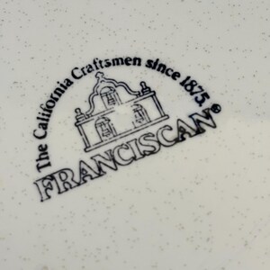 K&ouml;nnte beinhalten: Nahaufnahme einer wei&szlig;en Keramikoberfl&auml;che mit einem gesprenkelten Muster. Das Bild zeigt ein schwarz-wei&szlig;es Logo mit der Aufschrift "The California Craftsmen since 1875. FRANCISCAN" mit einer Illustration eines Geb&auml;udes.