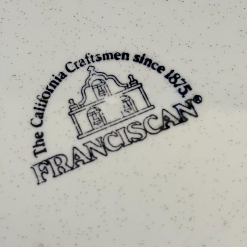 K&ouml;nnte beinhalten: Nahaufnahme einer wei&szlig;en Keramikoberfl&auml;che mit einem gesprenkelten Muster. Das Bild zeigt ein schwarz-wei&szlig;es Logo mit der Aufschrift "The California Craftsmen since 1875. FRANCISCAN" mit einer Illustration eines Geb&auml;udes.