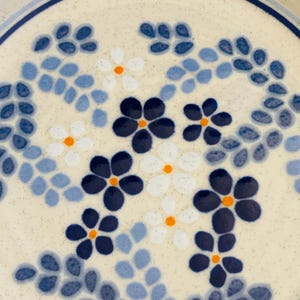K&ouml;nnte beinhalten: Nahaufnahme eines Keramiktellers mit cremefarbenem, gesprenkeltem Hintergrund. Der Teller hat ein Blumendesign mit dunkelblauen, hellblauen, wei&szlig;en und orangefarbenen Blumen. Der Rand des Tellers hat einen dunkelblauen Rand.