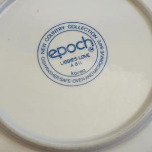 K&ouml;nnte beinhalten: Nahaufnahme eines wei&szlig;en Keramiktellers mit blauem Rundstempel. Der Stempel lautet "epoch" und "LIBBIES LOVE A811 Korea". Der Teller geh&ouml;rt zur "NEW COUNTRY COLLECTION" und ist sp&uuml;lmaschinen-, ofen- und mikrowellengeeignet.