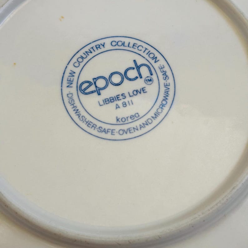 K&ouml;nnte beinhalten: Nahaufnahme eines wei&szlig;en Keramiktellers mit blauem Rundstempel. Der Stempel lautet "epoch" und "LIBBIES LOVE A811 Korea". Der Teller geh&ouml;rt zur "NEW COUNTRY COLLECTION" und ist sp&uuml;lmaschinen-, ofen- und mikrowellengeeignet.