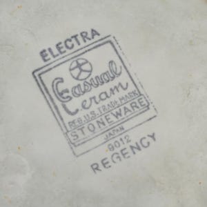 K&ouml;nnte beinhalten: Nahaufnahme einer wei&szlig;en Keramikoberfl&auml;che mit einem grauen Stempel. Der Stempel lautet oben "ELECTRA", mit "Casual Ceram STONEWARE" in einem rechteckigen Rahmen. Darunter steht "JAPAN - 9012 REGENCY."