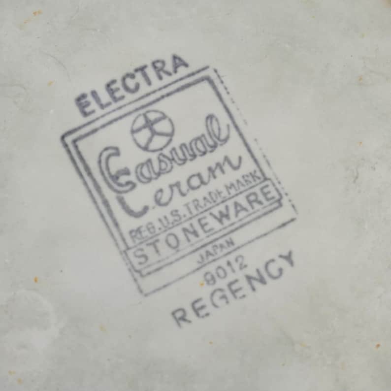 K&ouml;nnte beinhalten: Nahaufnahme einer wei&szlig;en Keramikoberfl&auml;che mit einem grauen Stempel. Der Stempel lautet oben "ELECTRA", mit "Casual Ceram STONEWARE" in einem rechteckigen Rahmen. Darunter steht "JAPAN - 9012 REGENCY."