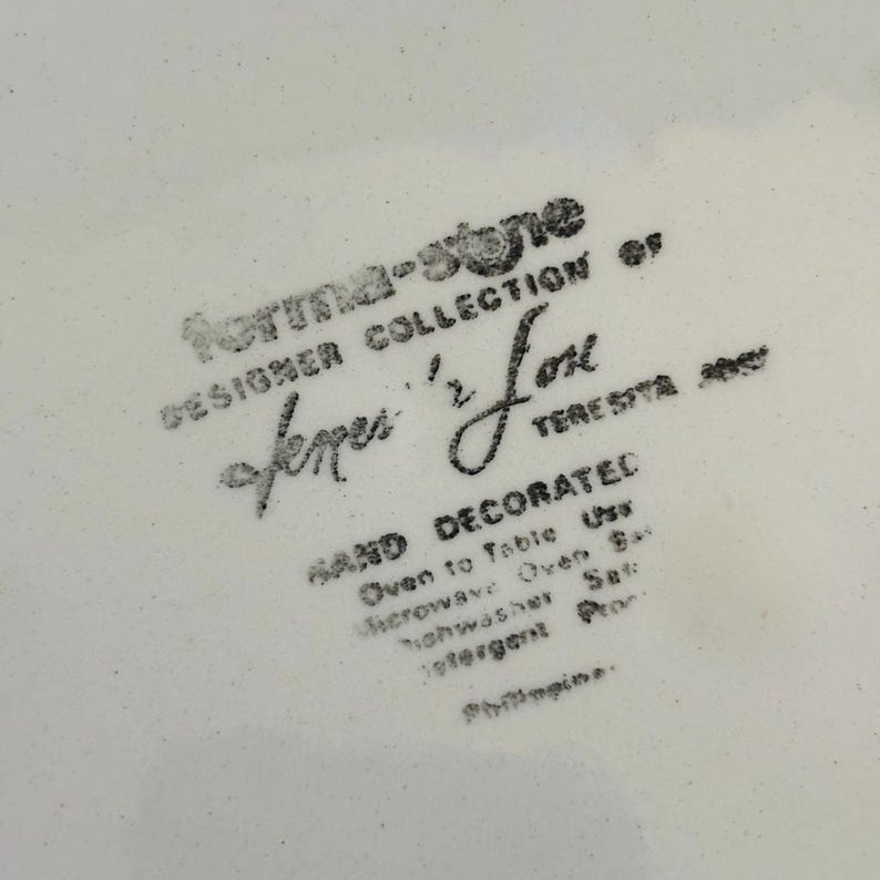 K&ouml;nnte beinhalten: Nahaufnahme eines wei&szlig;en Keramiktellers mit schwarzem Text. Der Text lautet "forma-stone DESIGNER COLLECTION of fermer '2' Love TERESITA". Zus&auml;tzlicher Text weist darauf hin, dass der Teller handdekoriert, ofen- und mikrowellengeeignet und sp&uuml;lmaschinenfest ist.