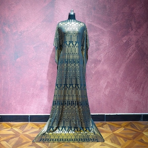 Puede incluir: Un vestido largo tipo caftán negro con un estampado geométrico dorado, exhibido en un maniquí. El vestido tiene mangas anchas y una silueta fluida. El patrón dorado es detallado y cubre toda la prenda.