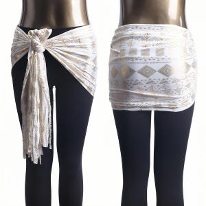 Puede incluir: Dos pañuelos de cadera blancos y dorados. Uno está anudado con una larga franja, el otro es un envoltorio ajustado. El patrón dorado incluye formas geométricas. Los pañuelos se muestran en un maniquí con leggings negros.