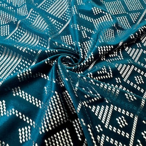 Puede incluir: Tela color turquesa con un patrón geométrico plateado. La tela está drapeada, mostrando la textura y el diseño. El patrón consiste en pequeñas formas y líneas repetidas, creando un efecto texturizado. La tela tiene una apariencia suave y aterciopelada.