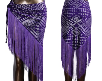 May include: A purple dance skirt with a geometric pattern and long fringe. The skirt is wrapped around a mannequin, showcasing the design and texture. The fringe hangs down, adding movement and flair to the garment.