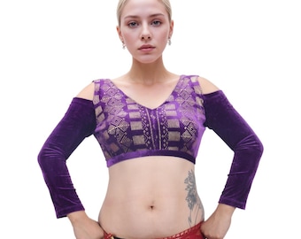 May include: A purple velvet crop top with long sleeves and a V-neck. The bodice features a gold geometric pattern. The sleeves are detached at the shoulders. The top is designed for belly dancing or similar performances.