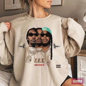 Op de afbeelding: Een set van drie keramische mokken met een gespikkelde, crèmekleurige glazuur. Elke mok heeft een ander handgeschilderd bloemmotief in tinten blauw, groen en geel. De mokken hebben een eenvoudige, moderne vorm.