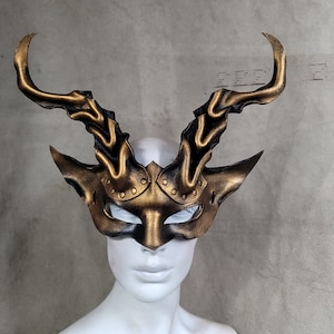 Peut inclure: Un masque de bal masqué en cuir noir et doré avec des cornes. Le masque a un design détaillé et est parfait pour une fête costumée ou un bal masqué.