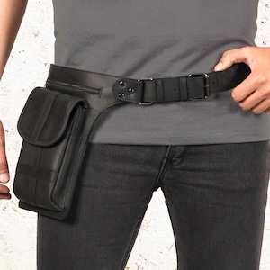Puede incluir: Cintur&oacute;n de cuero negro con un bolsillo y cierre de hebilla. El cintur&oacute;n presenta un bolsillo rectangular con solapa y costuras verticales. El cintur&oacute;n se lleva alrededor de la cintura y se combina con vaqueros negros.