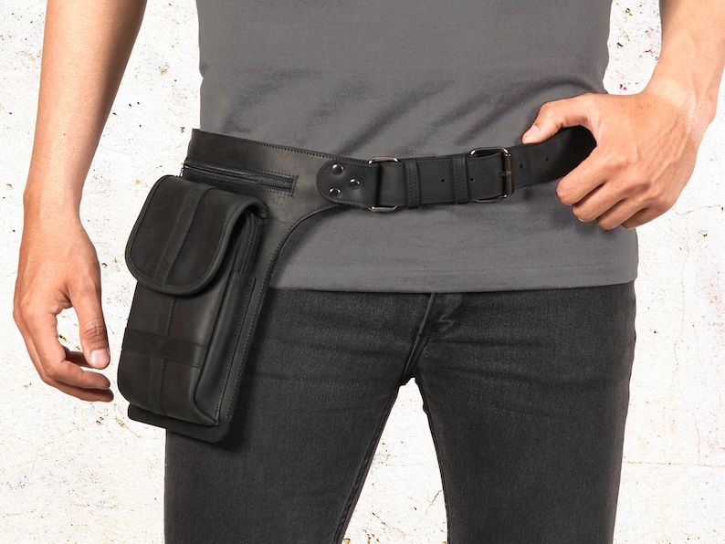 Puede incluir: Cintur&oacute;n de cuero negro con un bolsillo y cierre de hebilla. El cintur&oacute;n presenta un bolsillo rectangular con solapa y costuras verticales. El cintur&oacute;n se lleva alrededor de la cintura y se combina con vaqueros negros.