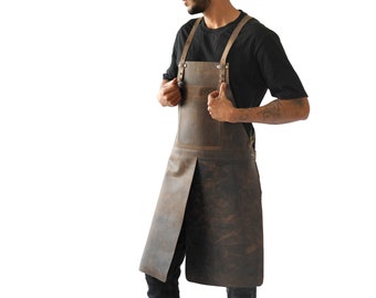 May include: A brown leather apron with adjustable straps and a front pocket. The apron is designed for full coverage and features a split at the bottom for ease of movement. The leather has a distressed finish.