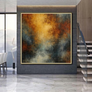 Könnte beinhalten: Großformatiges abstraktes Gemälde mit goldenem Rahmen. Das Kunstwerk zeigt eine Mischung aus Farben, darunter Orange, Braun, Türkis und Schwarz, die einen strukturierten, atmosphärischen Effekt erzeugen. Das Gemälde hängt an einer grauen Wand in einem modernen Innenraum.