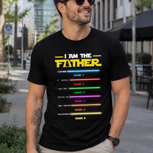 Może przedstawiać: Czarny t-shirt z napisem "I AM THE FATHER" w kolorze ż&oacute;łtym i serią kolorowych mieczy świetlnych z możliwością dodania imion. Koszulka jest noszona przez osobę w okularach przeciwsłonecznych.