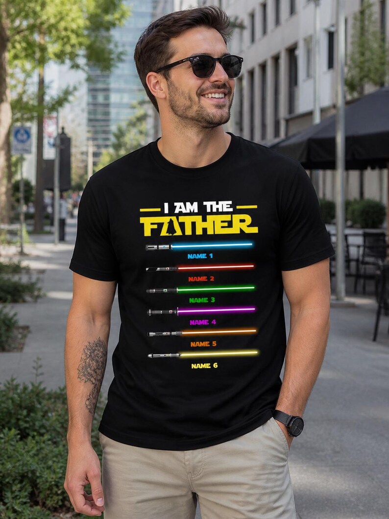Może przedstawiać: Czarny t-shirt z napisem "I AM THE FATHER" w kolorze ż&oacute;łtym i serią kolorowych mieczy świetlnych z możliwością dodania imion. Koszulka jest noszona przez osobę w okularach przeciwsłonecznych.