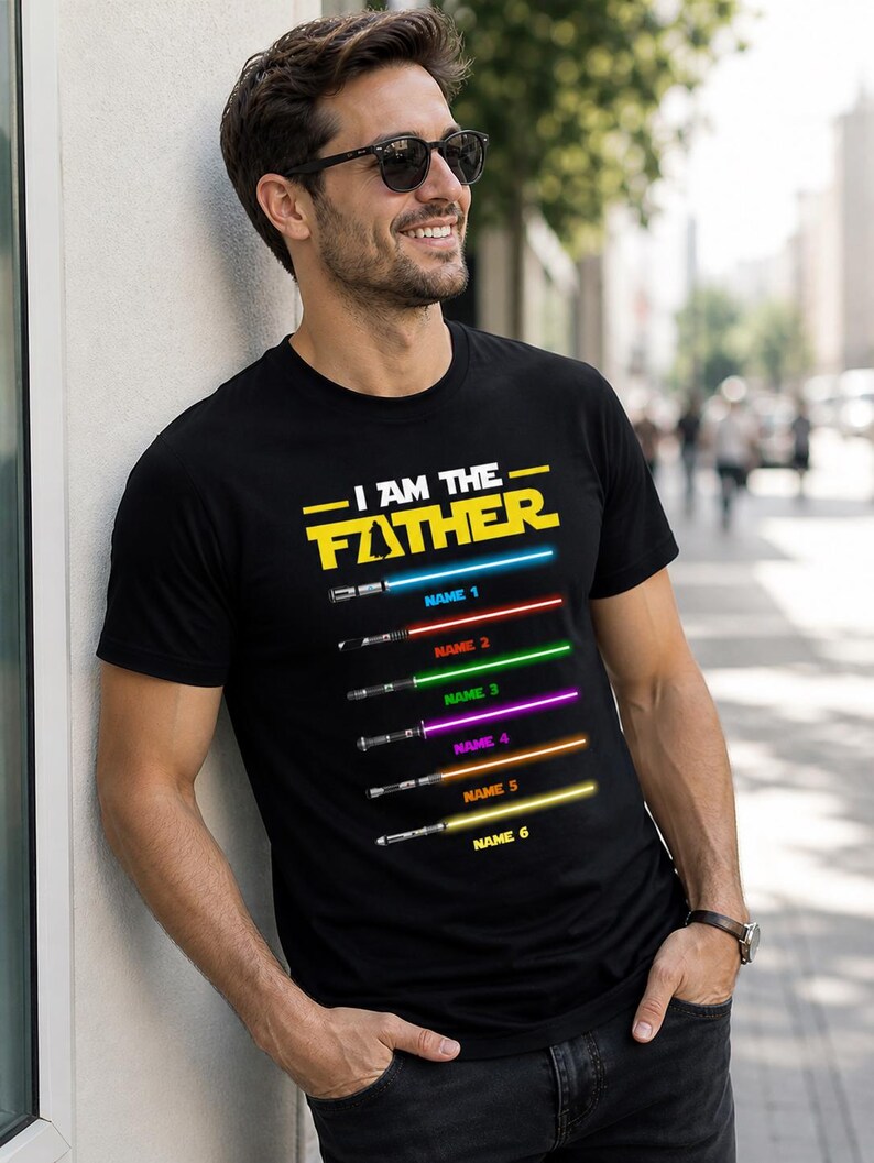 Może przedstawiać: Czarny t-shirt z napisem "I AM THE FATHER" w kolorze ż&oacute;łtym i białym. Poniżej tekstu znajduje się sześć mieczy świetlnych w r&oacute;żnych kolorach, każdy z nazwą. Osoba nosi okulary przeciwsłoneczne.