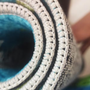 May include: Close-up of a rolled-up rug with a white, textured border. The rug's interior features a vibrant blue and green pattern. The white border is tightly stitched, creating a defined edge.