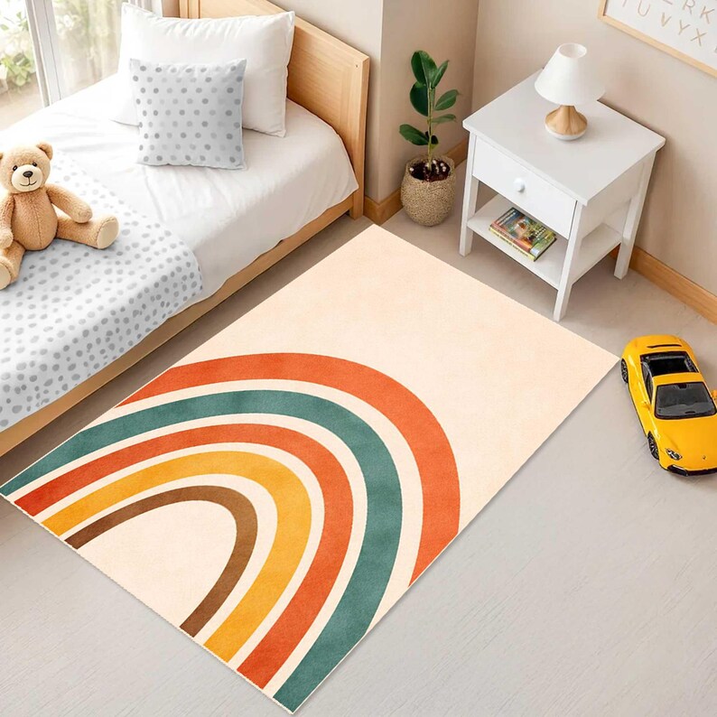 May include: A rectangular area rug featuring a large, centered rainbow graphic with concentric arches in shades of orange, teal, yellow, and brown against a light cream background. The rug is positioned on a floor in a room with a bed and furniture.