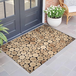 May include: Rectangular doormat with a wood slice design. The mat features a pattern of various-sized, light brown wood circles against a black background. The mat is placed in front of a dark gray door.
