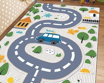 Op de afbeelding: Een rechthoekig kinderspeelkleed met een wegontwerp, met een blauwe auto, bomen, huizen en bloemen. De grijze weg heeft witte stippellijnen, tegen een gestreepte achtergrond. Ontworpen voor fantasierijk spel.