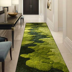 May include: A long, rectangular green rug with a textured, moss-like design. The rug features varying shades of green, creating a natural, organic pattern. The rug is placed in a hallway with a dark wooden door at the end.