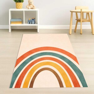 May include: A rectangular area rug featuring a centered, multi-colored rainbow graphic. The rainbow consists of concentric semi-circular bands in shades of burnt orange, muted teal, golden yellow, and dark brown against a cream-colored background.
