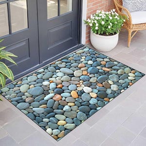 May include: Rectangular doormat featuring a pattern of smooth, colorful river stones. The stones are in shades of blue, gray, brown, and orange. The mat is placed in front of a dark gray door.