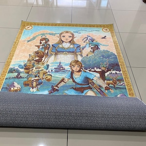 May include: A rectangular area rug featuring a colorful illustration of characters from The Legend of Zelda, including Link and Zelda, set against a landscape background. The rug has a gold border and a dark gray, textured non-slip backing material.