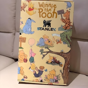 May include: A yellow box featuring illustrations of Winnie the Pooh characters, including Pooh, Eeyore, Tigger, and Piglet. The box has the text "Winnie the Pooh" and the Stanley logo. The box is decorated with images of the Hundred Acre Wood.