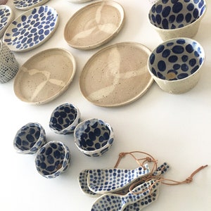 May include: A set of ceramic dishes and bowls with a blue and white polka dot pattern. The dishes are oval and round, and the bowls are round and have a slightly flared lip. There are also four small spoons with the same polka dot pattern.