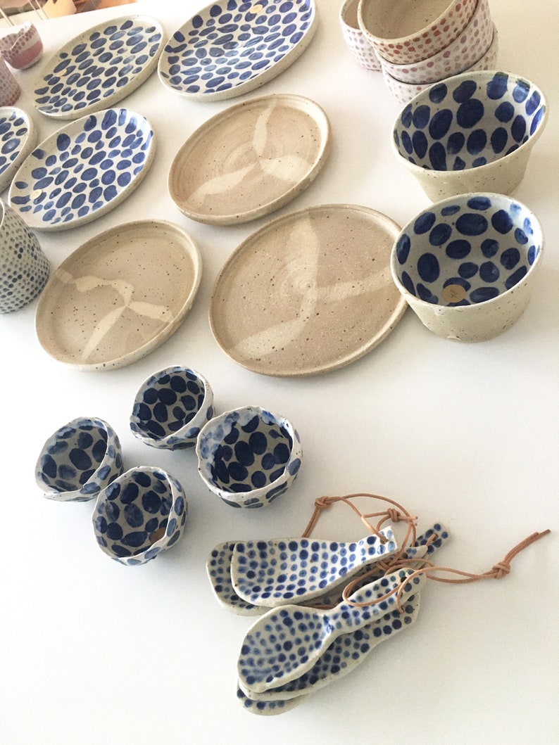May include: A set of ceramic dishes and bowls with a blue and white polka dot pattern. The dishes are oval and round, and the bowls are round and have a slightly flared lip. There are also four small spoons with the same polka dot pattern.